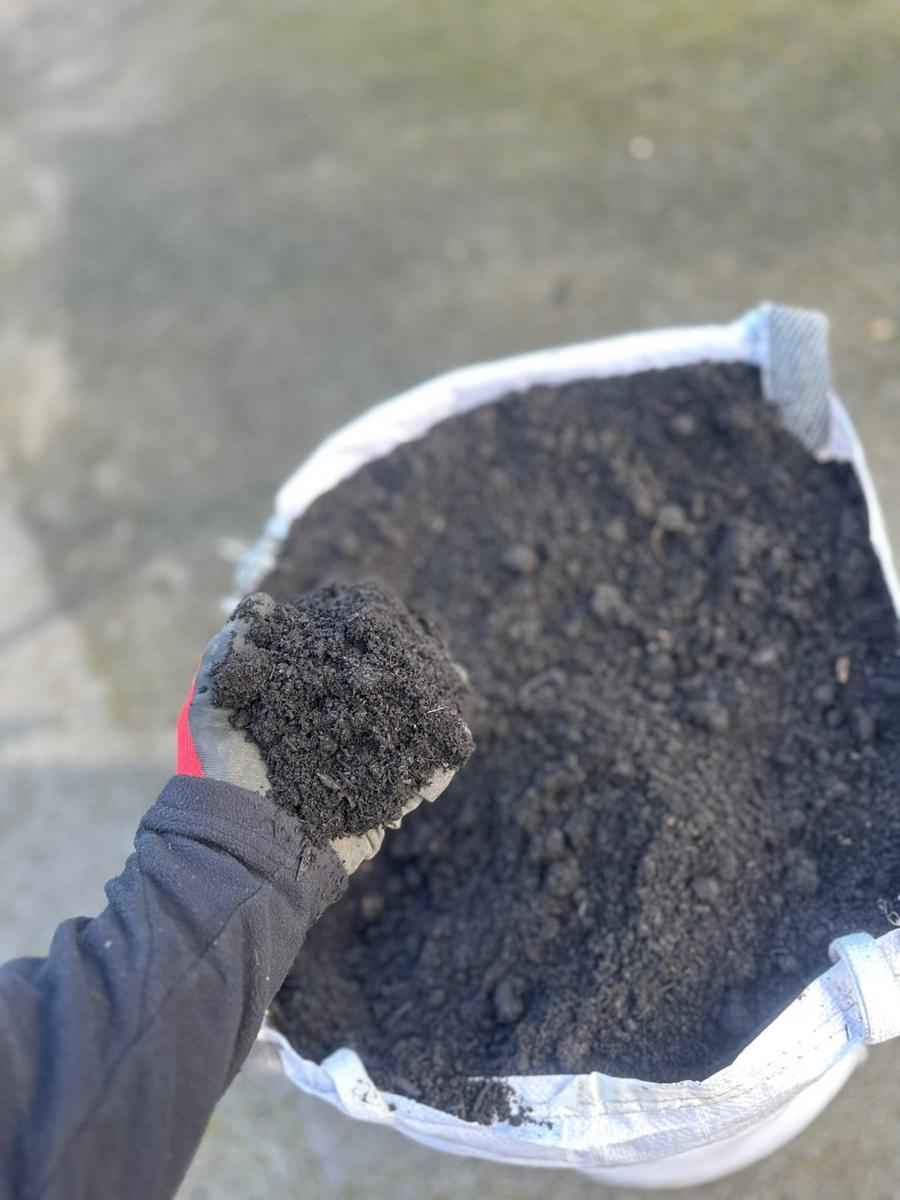 A handful of William Alexander peat-free compost over an open bag at the yard